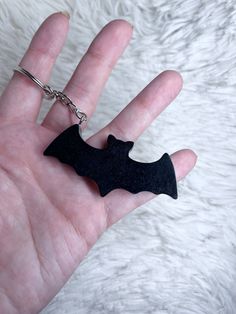 a hand holding a black bat shaped keychain on it's palm,