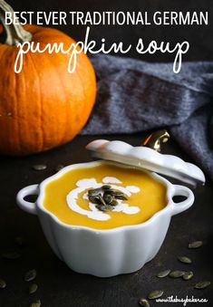 a white bowl filled with pumpkin soup next to a pumpkin and some seeds on the table