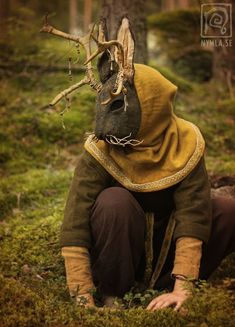 a person wearing a deer mask sitting in the grass next to a tree with no leaves on it