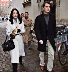 a man and woman are walking down the street with their bicycles behind them as people look on