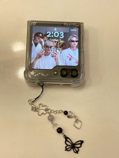 a cell phone with a chain attached to it and a butterfly charm hanging from the back