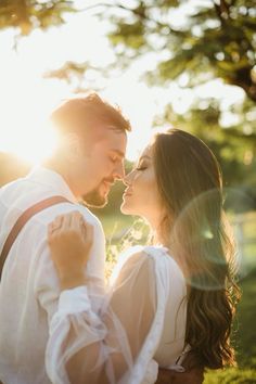 a man and woman standing next to each other in front of some trees with the sun shining on them