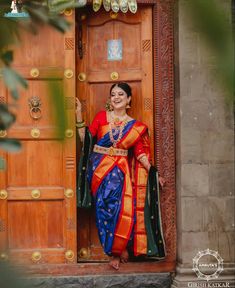 a woman in a blue and orange sari is standing on the door way to her home