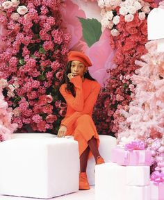 a woman in an orange dress and red hat sitting on a white box surrounded by pink flowers