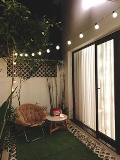 a chair and table are on the grass in front of an open door with white curtains