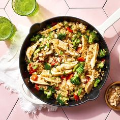 a skillet filled with chicken and vegetables next to two glasses of green smoothie