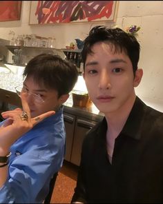 two young men sitting at a table with food and drinks in front of them, posing for the camera