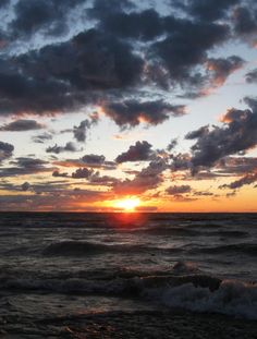 the sun is setting over the ocean with clouds