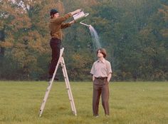 two men are standing on ladders and one is watering the grass