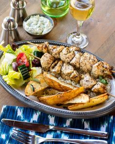 a plate with chicken, potatoes and salad on it next to two glasses of wine