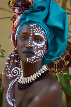 a woman with painted face and headdress poses for the camera while holding her hands to her face