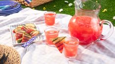 an outdoor picnic with drinks and snacks on the grass, including watermelon slices