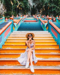 a woman sitting on the steps in front of colorful stairs with her hat and sunglasses