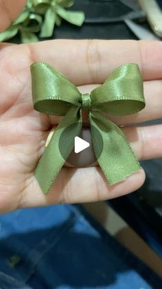 a hand holding a green bow on top of a piece of ribbon in it's palm