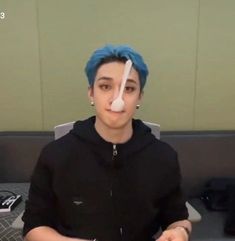 a man with blue hair and nose tape on his face is sitting in an office cubicle