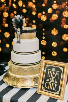 a three tiered cake with black and white stripes on the table next to a framed sign