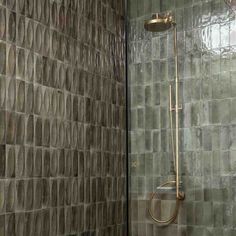 a shower with a glass door and tiled walls in a bathroom that has green tiles on the wall