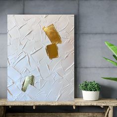 an abstract painting with gold paint on a white background next to a potted plant