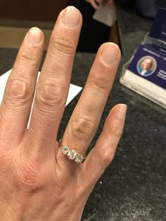 a woman's hand with a diamond ring on top of her finger, in front of a counter