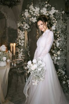 a woman in a wedding dress standing next to a table with flowers and candles on it