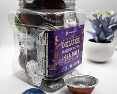 a jar filled with mixed nuts next to two bowls and a potted plant in the background