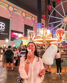 a woman standing in front of a ferris wheel eating food