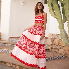 a woman in a red and white dress standing on steps near a cactus tree with her arms behind her back