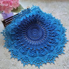 a blue crocheted doily sits next to a pink flower