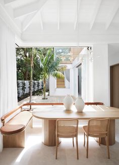 a dining room table with two white vases on top of it next to a bench