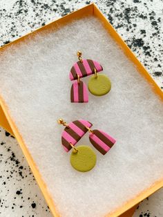 two pink and brown earrings sitting on top of a white box with snow in it