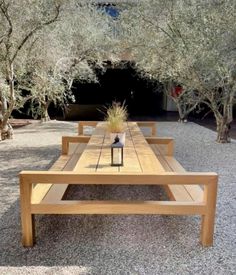 a wooden table sitting in the middle of a gravel covered area next to some trees