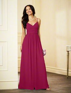 a woman in a long blue dress standing next to a white wall and smiling at the camera