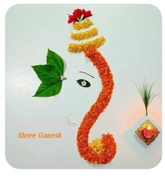 an artisticly decorated ganeshi decoration with leaves and flowers on the side of a white wall