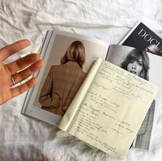 an open book with writing on it next to a hand holding a pen and paper