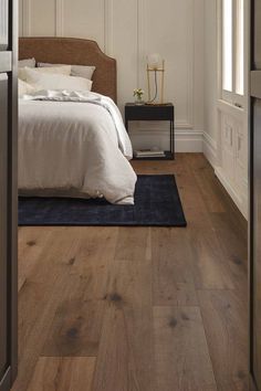 a bedroom with white walls and wood floors, along with a blue rug on the floor