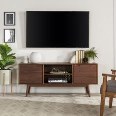 a flat screen tv mounted on the wall above a wooden entertainment center with books and plants