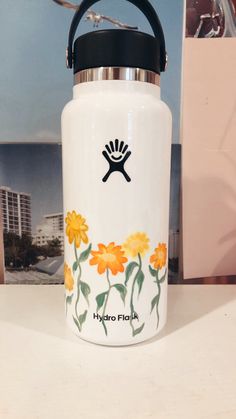 a hydro flask with flowers painted on it sitting on a table next to a photo