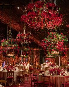 a room filled with lots of tables covered in red flowers and hanging chandeliers