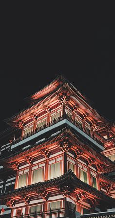 a tall building lit up at night with red lights on it's roof and windows