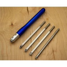 four different tools are laying on a wooden surface together, including a blue pen and two metal tips