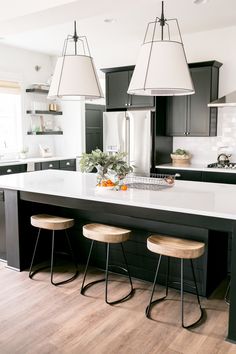 a kitchen island with three stools in front of it and two lights hanging from the ceiling