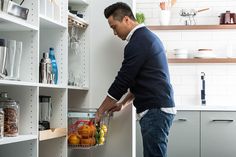 a man is holding a basket full of fruit in the middle of a kitchen pantry