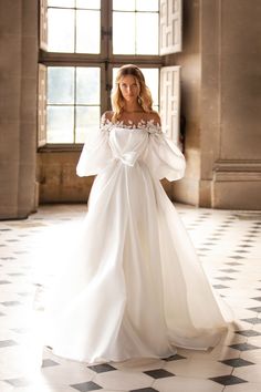 a woman in a white wedding dress standing on a checkered floor with an open window behind her