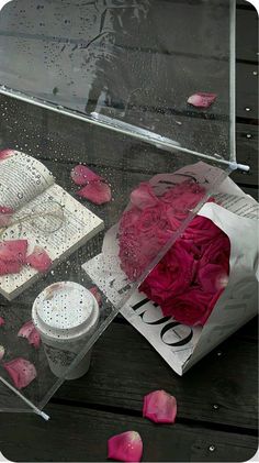 an open umbrella sitting on top of a wooden table next to flowers and books in the rain