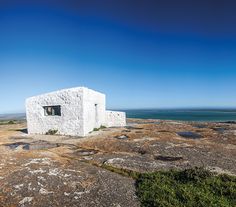 a small white building sitting on top of a rocky hill next to the ocean and blue sky