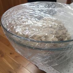 a clear glass bowl filled with dough on top of a wooden table covered in plastic