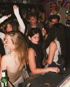 a group of young people standing around each other at a club or bar with their arms in the air