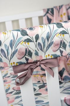 a baby crib bed with pink and blue flowers on it, along with a bow tie