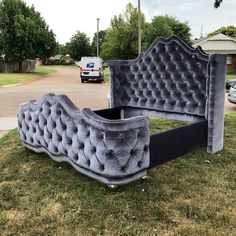 an upholstered bed is sitting in the middle of some grass near a street