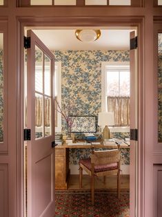 an open door leading into a room with floral wallpaper on the walls and desk